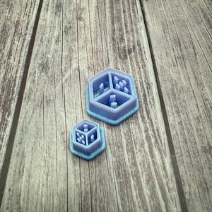 May include: Two purple 3D printed hexagonal dice with different patterns on each side.