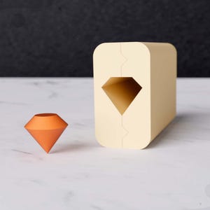 May include: A light orange diamond-shaped object sits on a white surface next to a beige block with a diamond-shaped cutout.