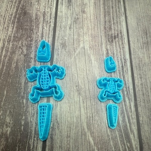 May include: Two sets of blue plastic cookie cutters shaped like alligators. The larger set has a head, body, and tail. The smaller set has a head, body, and tail.