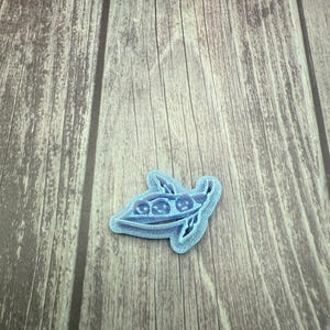 May include: A light blue pea pod cookie cutter. The cutter features a detailed design of a pea pod with three peas inside. The cutter is made of plastic and is designed for use with cookie dough or fondant. The cutter is approximately 3 inches long.