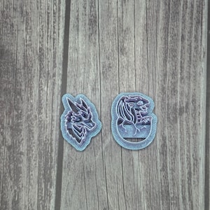May include: Two cookie cutters, one shaped like a dragon head and the other shaped like a dragon with its wings spread out. Both cutters are a light blue color with a purple tint.