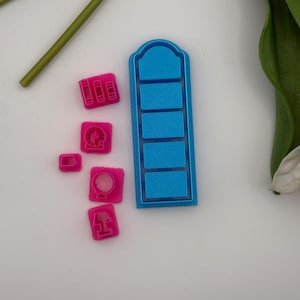 May include: A collection of pink and blue polymer clay cutters in various shapes. The cutters include a stack of books, a clock, a lamp, and a rectangular shape with four rectangular cutouts. The cutters are for crafting.