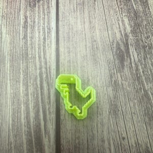 May include: A green plastic cookie cutter shaped like a pixelated dinosaur.