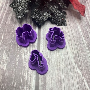 May include: Three purple plastic cookie cutters shaped like a cloud, a unicorn, and a flower.