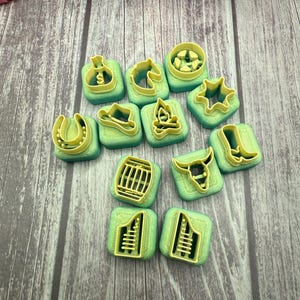 May include: A set of 12 green and yellow plastic cookie cutters shaped like various western themed items, including a horseshoe, cowboy hat, campfire, bull skull, and a barrel.
