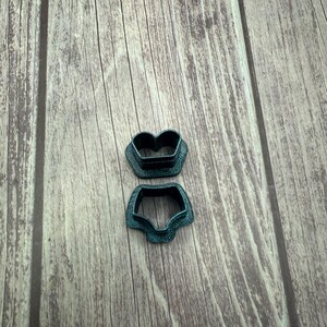 May include: Two teal-colored cookie cutters in the shape of a pair of underwear. The cutters are made of plastic and have a textured surface. They are placed on a wooden surface.