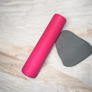 May include: A pink yoga mat with a textured surface and a gray yoga block.