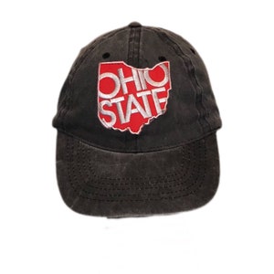 May include: A dark gray baseball cap with a curved brim. The front of the cap features a red and white embroidered design of the state of Ohio with the words "OHIO STATE" in white.