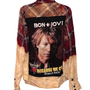 Może przedstawiać: Koszula flanelowa w kratę czerwoną i brązową z czarną naszywką z tyłu. Naszywka przedstawia zdjęcie Jona Bon Jovi i tekst "Bon Jovi" oraz "Because We Can World Tour".