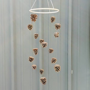 May include: A wooden ring mobile with brown pine cones hanging from it. The mobile is suspended from the ceiling.