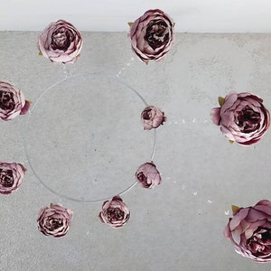 Puede incluir: Un móvil de flores rosa con nueve peonías falsas colgando de un aro de plástico transparente. Las flores están suspendidas del aro con un hilo transparente.