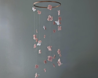 May include: A pink and white flower mobile with a wooden ring. The mobile features a variety of pink flowers and white butterflies hanging from strings.