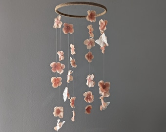 May include: A pink and white flower mobile with a wooden ring. The mobile has multiple strands of string with paper flowers hanging from them.