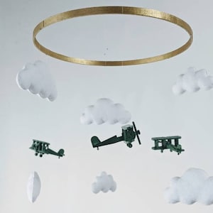 May include: A white and gold mobile with green airplanes and white clouds hanging from a gold ring.