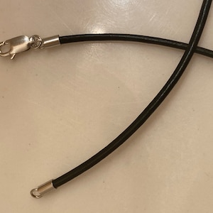 May include: A black leather cord necklace with silver clasps. The cord is about 2mm thick.