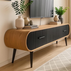 May include: A contemporary TV stand with a light wood finish and black ribbed drawer fronts. The stand has curved edges and dark legs. Vases and books are displayed on top. The unit is approximately 150 cm long.