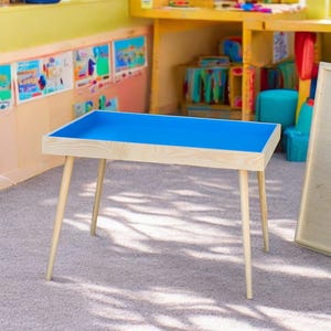 May include: A wooden table with a blue top and four legs. The table is in a classroom setting with a whiteboard leaning against the wall.