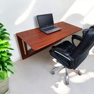 Peut inclure: Un bureau mural en bois foncé avec un ordinateur portable sur le dessus. Une chaise de bureau noire à roulettes est placée devant le bureau.