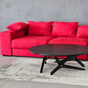 May include: A black round coffee table with a unique X-shaped base sits in front of a red sofa with multiple pillows.