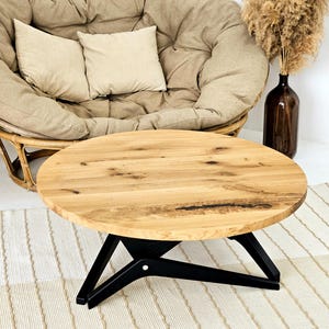 May include: A round wooden coffee table with a natural wood grain finish. The table has a black, geometric base. The table is approximately 36 inches in diameter and is a centerpiece in a cozy living space.