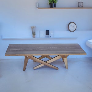 May include: A light wood coffee table with a unique X-shaped base. The table has a rectangular top and is made of natural wood.
