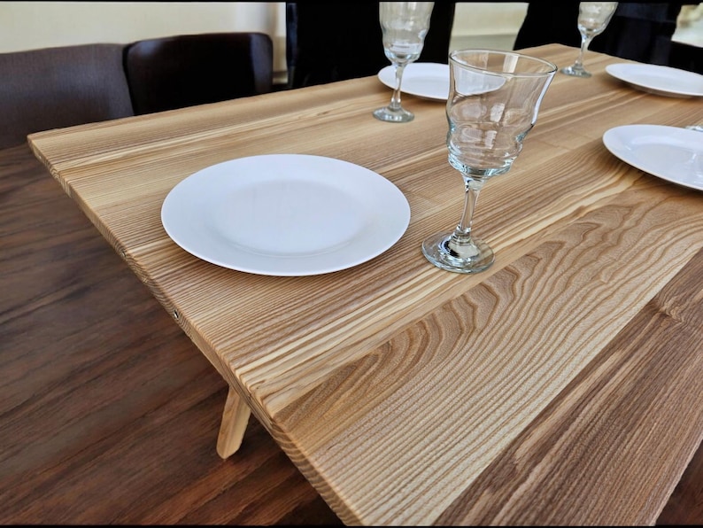 May include: A wooden table with a light brown finish. There are two white plates and three wine glasses on the table.