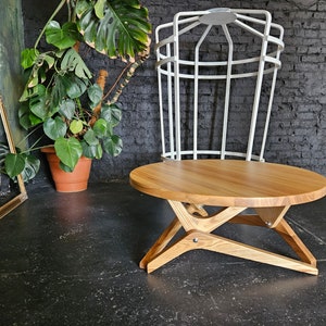 May include: A round wooden coffee table with a natural wood finish and a unique X-shaped base. The table is made of solid wood and has a smooth, polished surface.