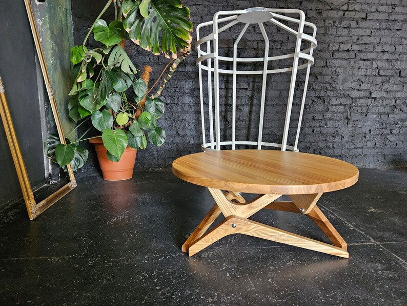 May include: A round wooden coffee table with a natural wood finish and a unique X-shaped base. The table is made of solid wood and has a smooth, polished surface.