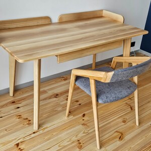 May include: A light wood desk with a drawer and a matching chair with a gray fabric seat. The desk has a simple design with rounded edges and straight legs. The chair has a similar design with a slightly curved back and straight legs.