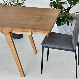 Puede incluir: Una mesa de madera con una extensi&oacute;n de hoja y una silla de tela gris con patas de metal negro. La mesa tiene un acabado marr&oacute;n claro y la silla tiene un dise&ntilde;o simple.