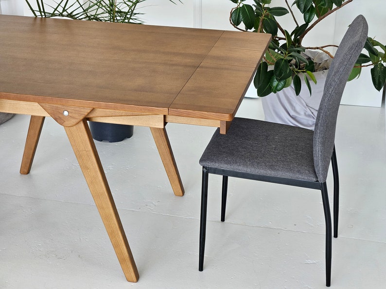 Puede incluir: Una mesa de madera con una extensi&oacute;n de hoja y una silla de tela gris con patas de metal negro. La mesa tiene un acabado marr&oacute;n claro y la silla tiene un dise&ntilde;o simple.