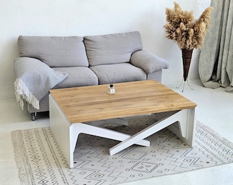 Può includere: Un moderno salotto con un divano grigio chiaro, un tavolino in legno con gambe bianche e un tappeto fantasia. Sono presenti anche un vaso decorativo con piante essiccate e una piccola bottiglia diffusore.