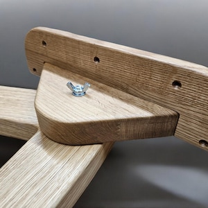 May include: Close-up of a wooden furniture piece with a triangular support and a metal nut. The wood is light brown and has a natural grain pattern.
