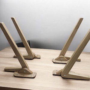 May include: Four wooden table legs with a folding design. The legs are made of light brown wood and have a simple, minimalist style.