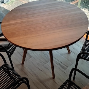 May include: A round wooden table with four black metal chairs. The table has a natural wood finish and the chairs have a slatted design.