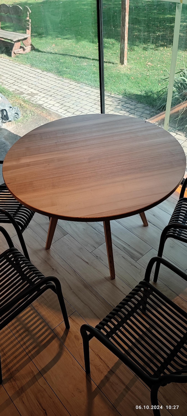 May include: A round wooden table with four black metal chairs. The table has a natural wood finish and the chairs have a slatted design.