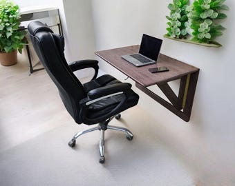 May include: A dark brown wooden wall-mounted desk with a laptop and a phone on the surface. A black office chair with wheels is in front of the desk.