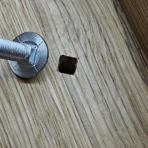 May include: Close-up of a silver metal screw with a round washer, partially inserted into a square hole in a piece of light brown wood.