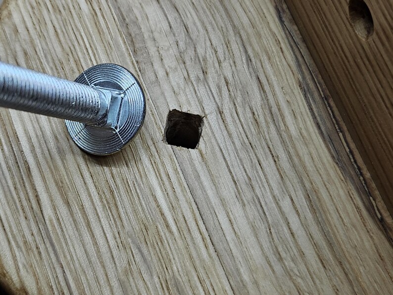 May include: Close-up of a silver metal screw with a round washer, partially inserted into a square hole in a piece of light brown wood.