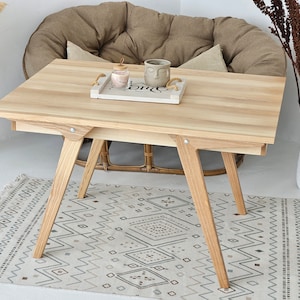 May include: A light wood table with a rectangular top and four legs. The table is sitting on a patterned rug in front of a brown chair.