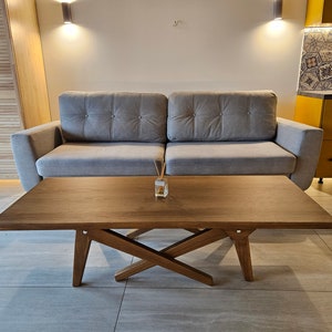 May include: A light gray sofa with a wooden coffee table in front of it. The coffee table has a criss-cross design and a light brown finish.