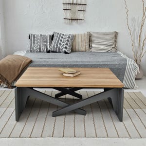 Könnte beinhalten: Ein Holz-Couchtisch mit schwarzem Metallgestell. Der Tisch hat eine rechteckige Tischplatte und ein Kreuzdesign an den Beinen. Der Tisch steht auf einem gestreiften Teppich vor einer Couch mit Kissen.