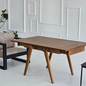 Puede incluir: Una mesa de madera marr&oacute;n con un caj&oacute;n y una silla de metal negro. La mesa tiene una tapa rectangular y cuatro patas. La silla tiene un asiento acolchado y un marco de metal negro.