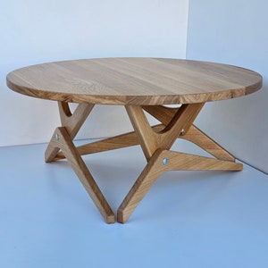 May include: A round wooden coffee table with a natural wood finish and a unique X-shaped base.
