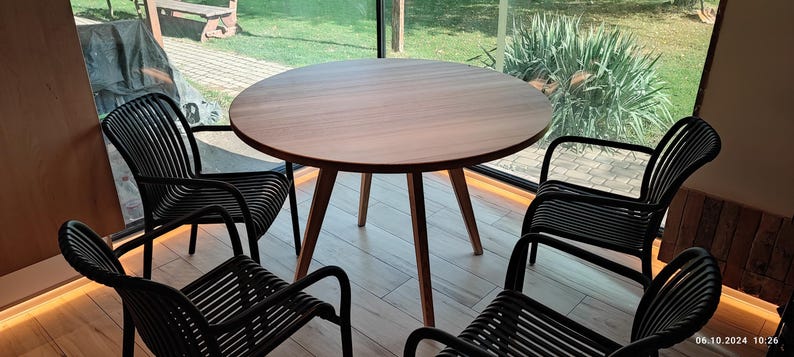 May include: A round wooden table with four black chairs. The table has a natural wood finish and the chairs have a woven design.