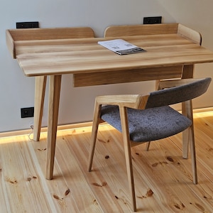 May include: A wooden desk with a drawer and a grey upholstered chair. The desk has a light wood finish and the chair has a simple design.