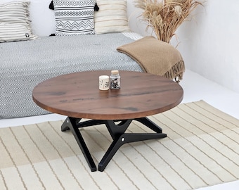 Könnte beinhalten: Ein runder, dunkelbrauner Couchtisch aus Holz mit einem schwarzen geometrischen Gestell. Der Tisch hat eine natürliche Holzmaserung und steht auf einem beige-weiß gestreiften Teppich. Zwei kleine Gläser stehen auf der Tischoberfläche.