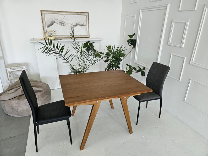 Puede incluir: Una mesa de comedor de madera con una tapa marr&oacute;n y cuatro patas. Dos sillas est&aacute;n colocadas en la mesa, una con un asiento negro y la otra con un asiento gris.