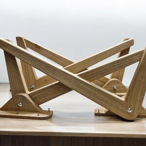 May include: A wooden table base with a unique X-shaped design. The base is made of light brown wood and has a natural finish. The base is designed to be used with a glass or wood tabletop.
