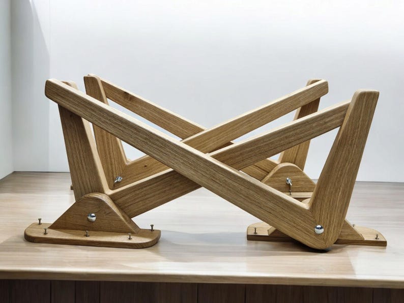May include: A wooden table base with a unique X-shaped design. The base is made of light brown wood and has a natural finish. The base is designed to be used with a glass or wood tabletop.